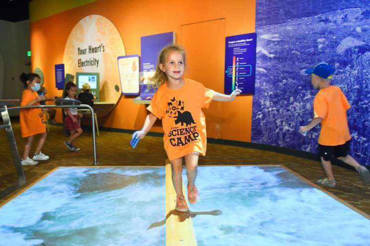 A young girl wearing an orange shirt explores an interactive floor, stepping on dynamic designs that respond to her movements.