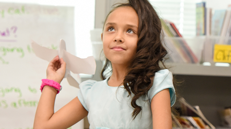 A young girl prepares to through a paper model of a bird