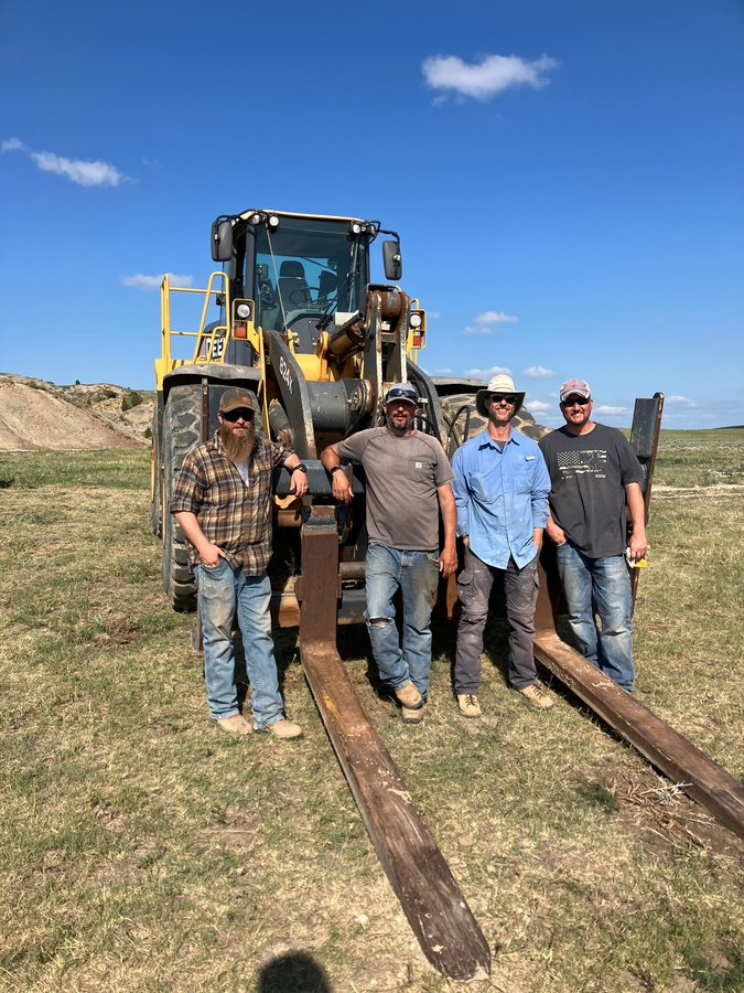 Dr. Tyler Lyson with his brother Derek Lyson and equipment operations team standing in front of a 60,000-pound front loader to transport the jacket to the highway.
