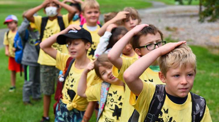 a class of children line up with their belongings to head inside and begin the camp day