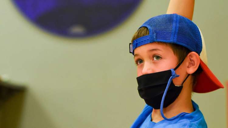 a student wearing a ball cap and a face mask raises their hand