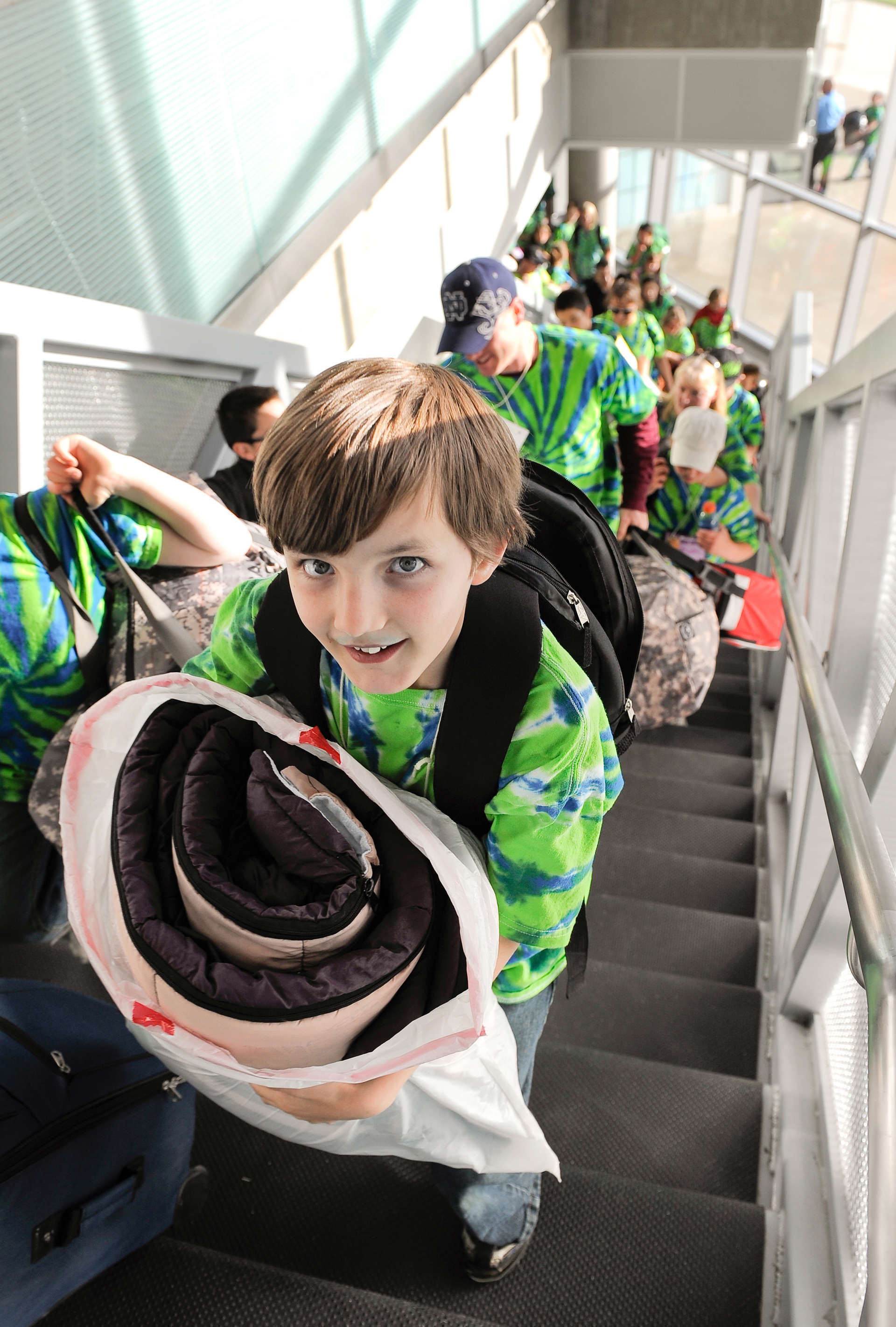 Student climb stairs carrying overnight gear.