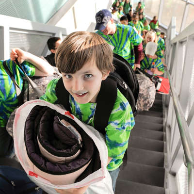 Children in green t-shirts bringing sleeping bags and items up stairs