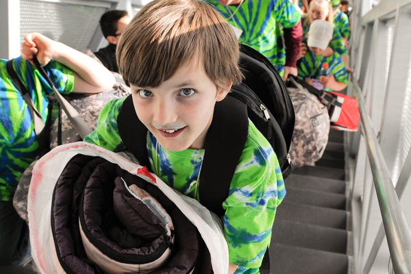 Children in green t-shirts bringing sleeping bags and items up stairs