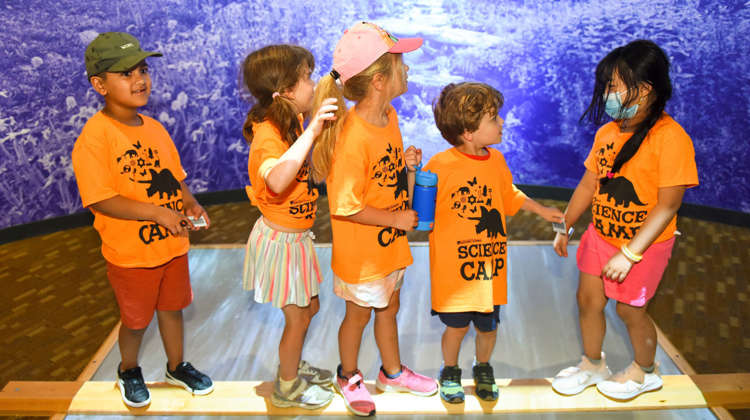 A group of children in orange shirts stands together on a wooden platform, smiling and enjoying their time in Expedition Health. .