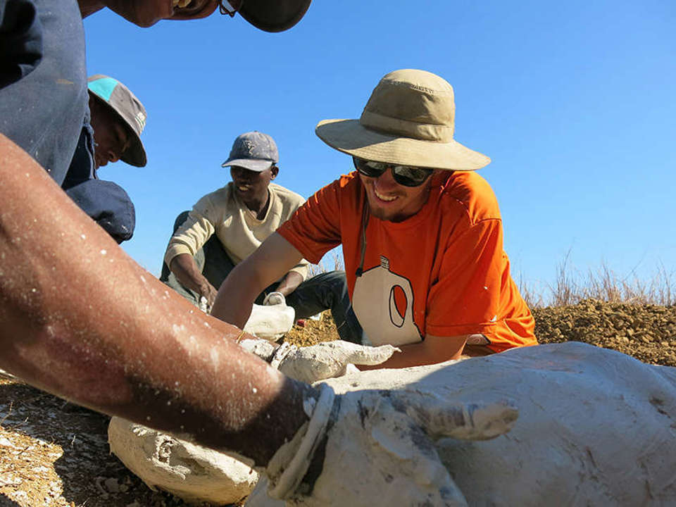 Four people working to add plaster to a field jacket, the main one smiling and wearing a hat and an orange shirt