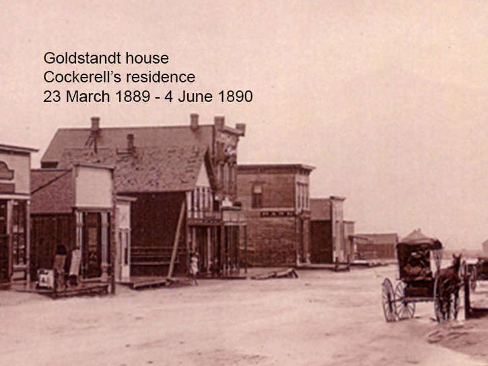 sepia toned image of a street in the late 1800s with a few buildings in the background