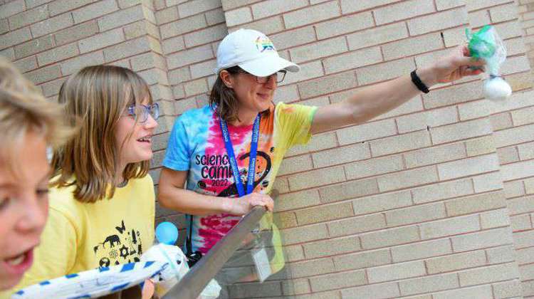 A teacher holds an egg over a landing, preparing an experiment observing the effects of gravity as students look on, cheering. 