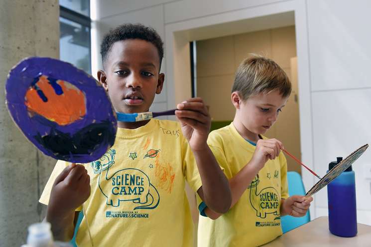 Two young boys in yellow shirts joyfully holding paintbrushes, ready to create colorful artwork together.