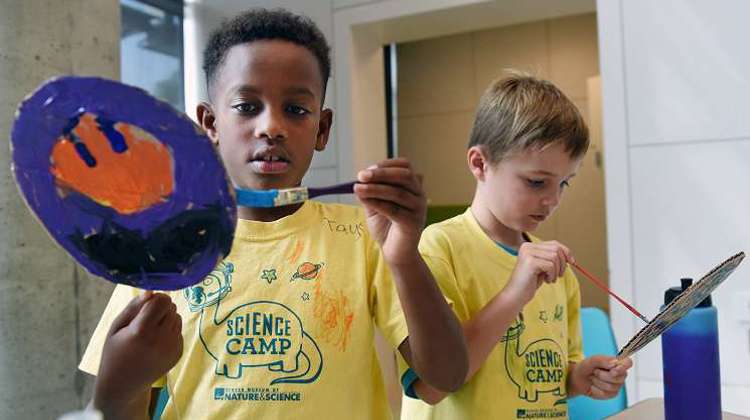 Two young boys in yellow shirts joyfully holding paintbrushes, ready to create colorful artwork together.