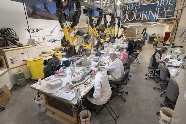 wide view of a preparation lab with many people working at a large table