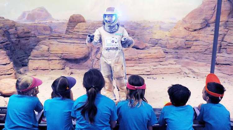 A person in a space suit engages with a group of children, sharing knowledge about space exploration and science.