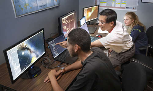 Two students sitting at computers with a mentor explaining what is on the screen