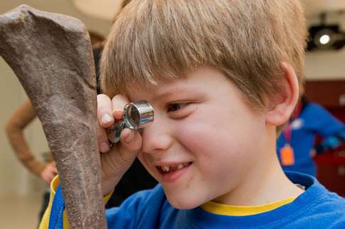 Child with short hair using a hand lens to look at the details in a fossilized bone