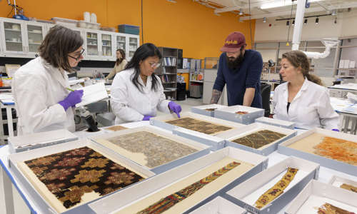Three women and one male researcher look at Archeological Textiles in the laboratory