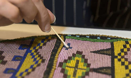 close up of a conservator using a Q-tip to clean a colorful beaded object