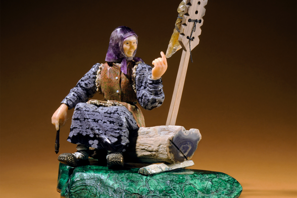 Gem carving called "The Grandmother": statue of a woman seated on a log, made of quartz, amethyst, obsidian, jasper, aragonite, gold plated silver, malachite, and petrified wood.