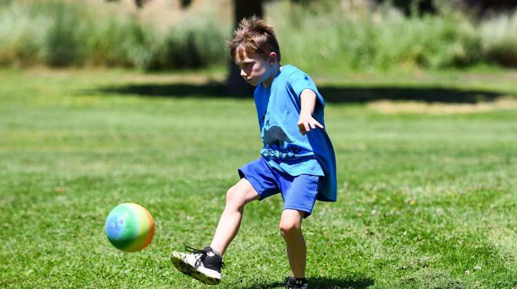 A boy in a blue t-shirt kicks a colorful ball, enjoying the weather outside