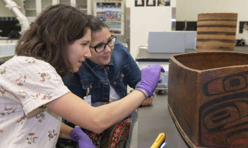 Conservator Megan Salas examines a wooden box with a tribal representative